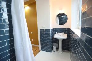 La salle de bains est pourvue de carrelage bleu, d'un lavabo et d'un miroir. dans l'établissement Le vintage 100 mètres de la gare parking gratuit, à Douai