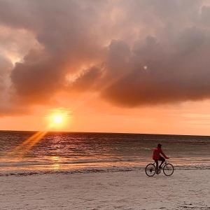 uma pessoa a andar de bicicleta na praia ao pôr-do-sol em Gadea Boutique Hotel& Gadea Garden Italian Restaurant em Jambiani