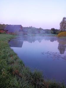 een waterlichaam met een huis op de achtergrond bij Mežvītoli in Mercendarbe