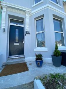 a white house with a black door and two potted plants at The Walnut Suite lovely one bedroom flat in Stoke. in Plymouth