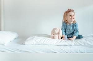 a little girl sitting on a bed with a stuffed animal at Ferienhaus am Mühlenweiher 2 in Leutkirch im Allgäu