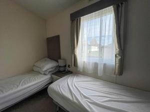 two beds in a small room with a window at Beautiful Caravan With Decking At California Cliffs In Scratby Ref 50052l in Great Yarmouth