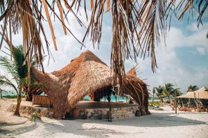 a straw hut on a beach with palm trees at GlampIKAL formerly Casa Nawal in Tulum