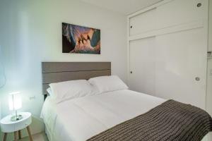 a white bedroom with a bed and a table and a lamp at Trankilidad Apartments in Santa Cruz