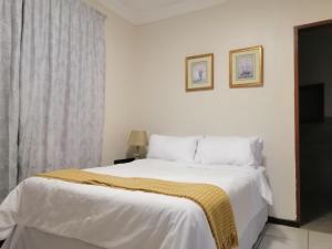a bedroom with a white bed with a yellow blanket on it at Villa Pretoria in Pretoria
