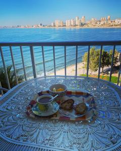 une table avec une assiette de nourriture et deux tasses de café dans l'établissement Coqueto apartamento sobre el mar, à El Campello
