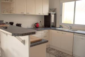 eine Küche mit weißen Schränken und schwarzen Arbeitsplatten in der Unterkunft Villa Hibiscus à 10 min de l'océan in Saubion