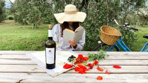 una mujer sentada en una mesa de picnic con una botella de vino en Agriturismo Fioralba, en Polpenazze del Garda