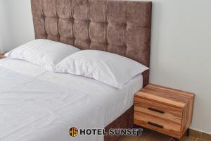 a bed with a brown headboard and a wooden night stand at Hotel SUNSET Shengjin in Shëngjin