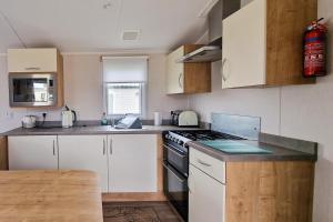a kitchen with white cabinets and a stove top oven at Lovely Caravan Nearby The Beach In Hunstanton, Norfolk Ref 23071c in Hunstanton