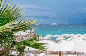 una spiaggia con ombrelloni bianchi e barche in acqua di Butterfly-Palais des Festival-center-quiet-AC-Wi Fi parking a Cannes