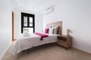 a white bedroom with a large bed with pink pillows at La Puerta del Mar - Alicante in Alicante