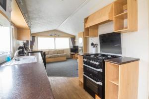 a kitchen with a stove and a couch in a room at 3 Bed, 8 Berth Caravan For Hire At St Osyth Park Near Clacton-on-sea Ref 28039cw in Clacton-on-Sea