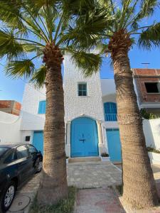 two palm trees in front of a house with a blue garage at Maison la perle de Hammam Sousse in Hammam Sousse