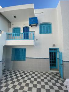 a white building with blue windows and a checkered floor at Maison la perle de Hammam Sousse in Hammam Sousse