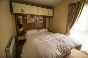 a bedroom with a large bed and a window at Lovely Caravan With Decking At Millfields Caravan Park Ref 87025f in Skegness