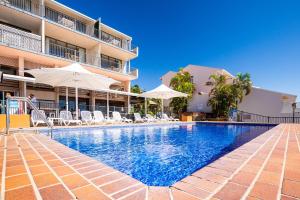 a swimming pool with chairs and umbrellas next to a building at OCEAN VIEWS 16 pool & Spa Wi-FI in Airlie Beach