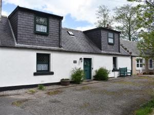 uma casa branca com um telhado preto e uma porta azul em Primrose Cottage em Elgin