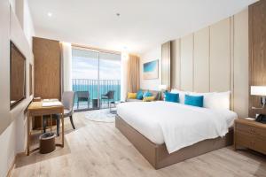 a hotel room with a large bed and a desk at Homie Panorama Beachfront Residences Nha Trang in Nha Trang