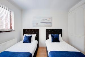 two beds in a white room with blue pillows at Great Location Free Parking Contractor Leisure in Peterborough