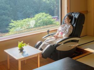 a woman sitting in a chair by a window at Hotel Oyanagi in Tagami