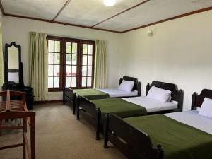 a room with three beds with green sheets and windows at The Green Savanna Holiday Bungalow Nuwara Eliya in Nuwara Eliya
