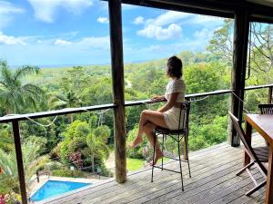 a woman sitting on a chair on a porch looking out at the forest at The Junglehouse Noosa in Doonan