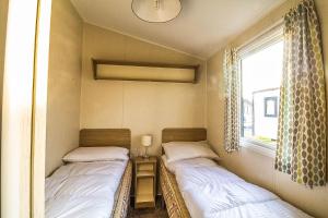 Duas camas num pequeno quarto com uma janela em Caravan With Decking At Highfield Grange In Essex Ref 26452ba em Clacton-on-Sea