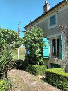 an old house with a blue window and bushes at Charmant studio avec jardin à la campagne sur le chemin de Saint Jacques de Compostelle in Lauzerte