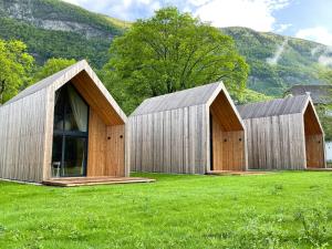 three wooden buildings in a field with mountains in the background at Cabino - Fresh Air Resort in Bovec