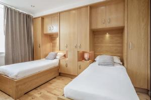 2 łóżka w pokoju z drewnianymi szafkami w obiekcie Luxe - Hyde Park - 2Bed 3Bath A/C + Lift w Londynie