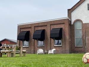 a brick building with black awnings and tables and chairs at Gastfabriek Tzummarum in Tzummarum