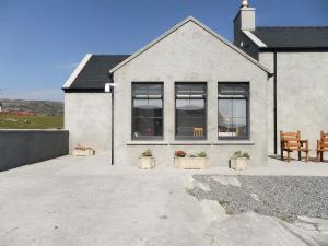 a white house with windows and a table and chairs at Kilbride Cottage in Pollachar