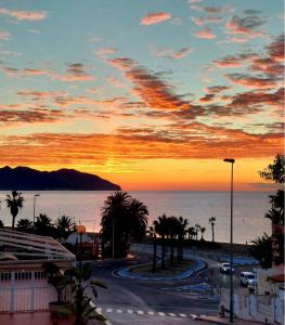 una puesta de sol sobre una calle con palmeras y el océano en Precioso Apartamento, en Puerto de Mazarrón