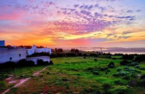 a sunset over a field with a building in the foreground at Maison de la Lagune in Oualidia