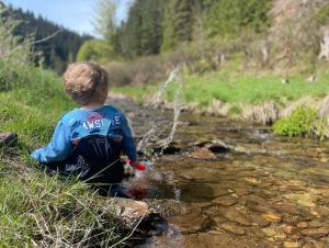 um rapaz sentado num riacho a brincar na água em Ebermannsmühle em Lauscha