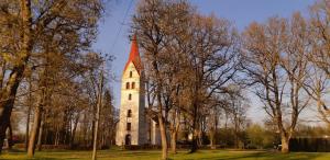 ein Gebäude mit einem Kirchturm auf einem Feld mit Bäumen in der Unterkunft Pärnu-Jaagupi pastoraat in Pärnu-Jaagupi