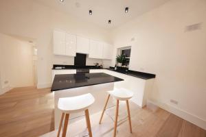 a kitchen with white cabinets and two white stools at Beautiful brand-new flat in London