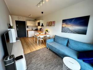 a living room with a blue couch and a kitchen at Apartament na Wydmie Gardenia Dziwnów in Dziwnów