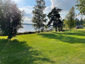 a field of grass with trees and a body of water at Idyllic Dalarna farmhouse at the lake in Leksand