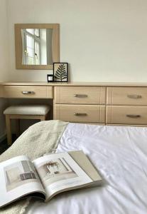 a book on a bed with a dresser and a mirror at Home in Solihull - Near NEC, BHX & Solihull Town Centre in Birmingham