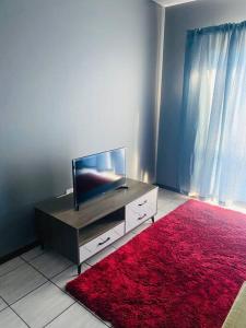 a living room with a television and a red rug at 2 bedroom apartment close to OR Tambo in Kempton Park