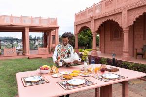 Eine Frau steht neben einem Tisch mit Essen drauf. in der Unterkunft StayVista at Pink Palace Rajasthani Decor in Udagamandalam + 20 Fotos