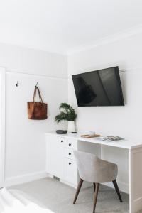 a white desk with a chair and a tv on a wall at Dormie House in Moss Vale