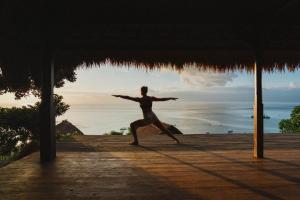 a woman doing a yoga pose on a dock with the ocean at Morin Resort in Nusa Lembongan