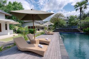 - une piscine avec des chaises et un parasol à côté d'une maison dans l'établissement Ariana Beach Resort Amed Bali, à Amed