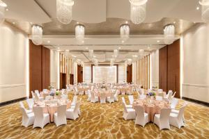 Crowne Plaza Shanghai Xiayang Lake, an IHG Hotel في Qingpu: قاعة احتفالات كبيرة مع طاولات بيضاء وكراسي بيضاء