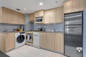 Una cocina con electrodomésticos de acero inoxidable y gabinetes de madera. en KozyGuru | Haymarket | 2B Apt With Amazing View | Walk To Darling Harbour, en Sídney