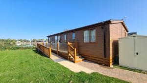 a small house with a deck next to a grass field at Tattershall Lakeside Lodge Indulgent wheelchair accessible 8 berth with Hot Tub in Tattershall