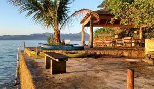 a house with a bench and a boat on the water at REFUGIO na frente do mar em Ilha de Araujo in Paraty